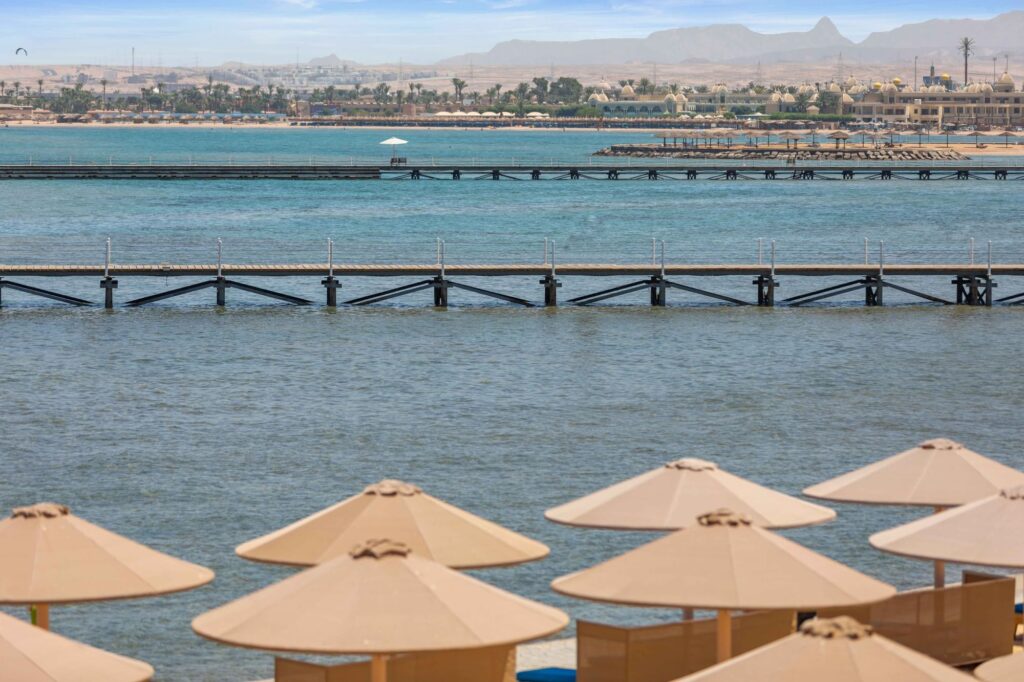 Sonnenschirme am Strand mit Blick auf das türkisfarbene Rote Meer und lange Holzstege vor der Küste von Hurghada.