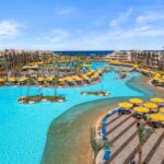 Große, geschwungene Poollandschaft mit gelben Sonnenschirmen, Palmen und Liegestühlen im Pickalbatros Palace Resort am Roten Meer.