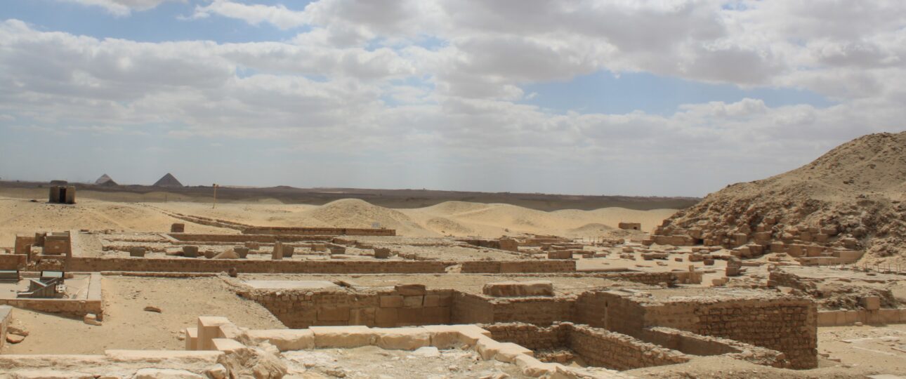 Freigelegte Mauerreste in der Nekropole von Sakkara mit Pyramiden am Horizont.